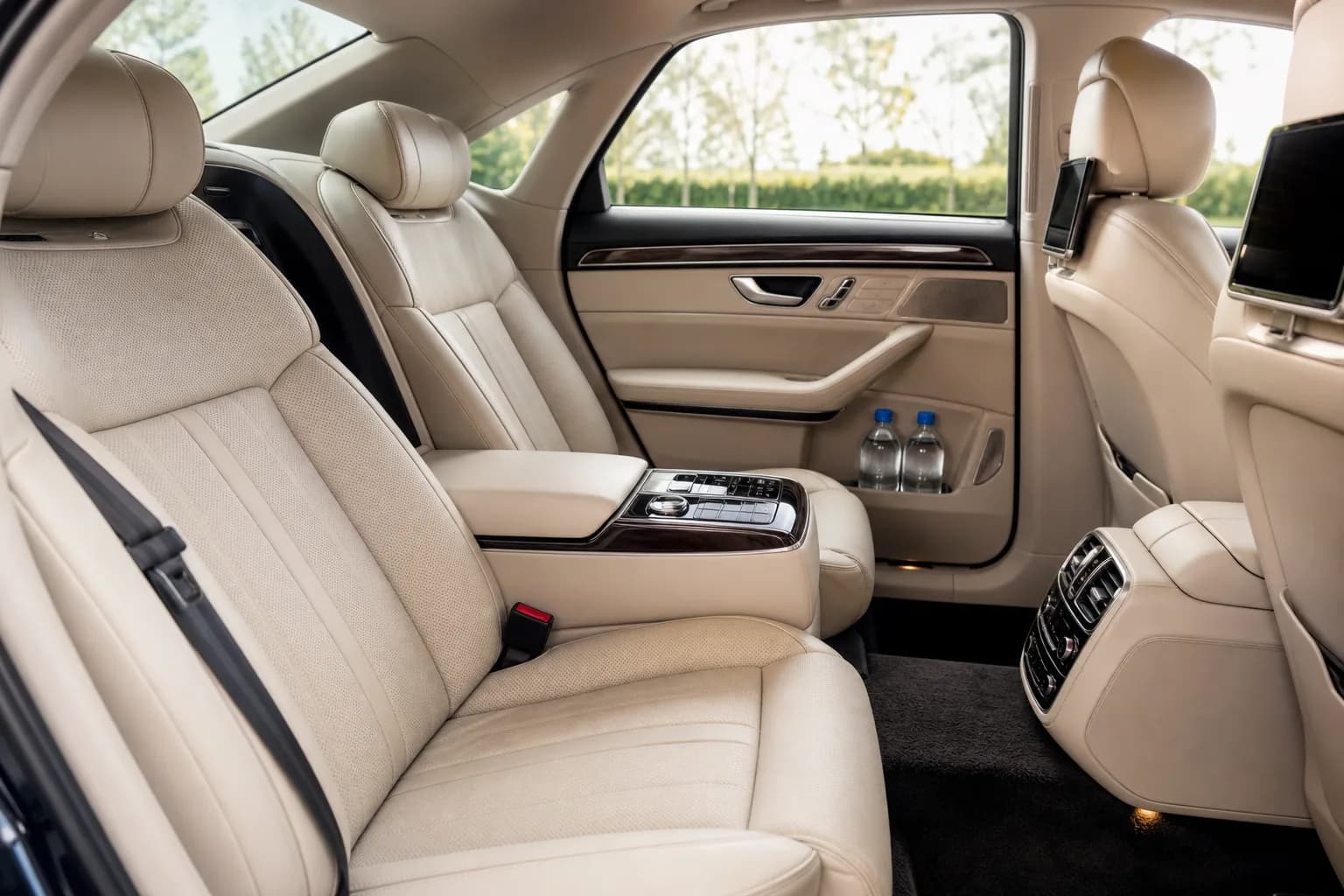 The cream leather rear cabin of a chauffeur-driven car, with climate controls and bottled water